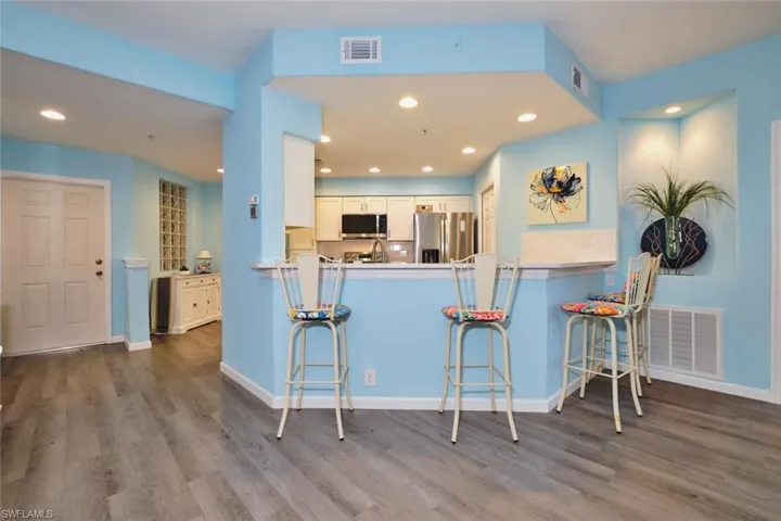 Kitchen with appliances with stainless steel finishes, wood finished floors, a peninsula, a kitchen breakfast bar, and recessed lighting