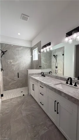 Bathroom featuring a marble finish shower, double vanity, and dark marble finish floors