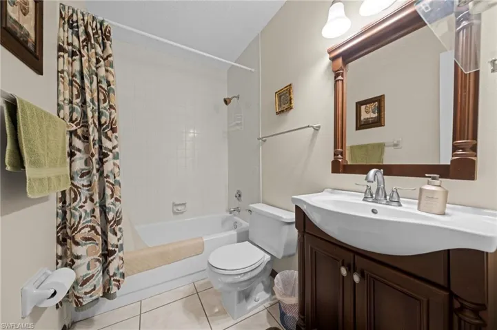 Bathroom featuring a dark wood vanity with an integrated white sink, a matching framed mirror, and a white tiled shower/tub combination with a wall-mounted showerhead