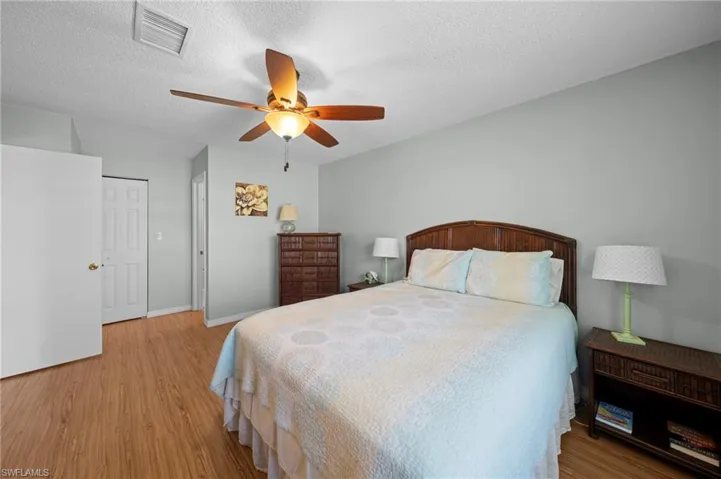 Bedroom featuring wood-finish flooring, a ceiling fan with integrated lighting, light-colored wall paint, and a white paneled door