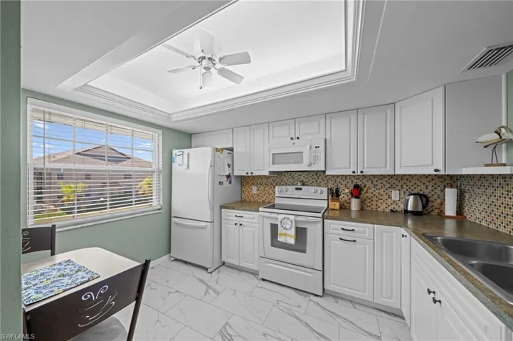 Kitchen featuring white cabinetry, a mosaic tile backsplash, solid surface countertops, white appliances, and large format floor tiling