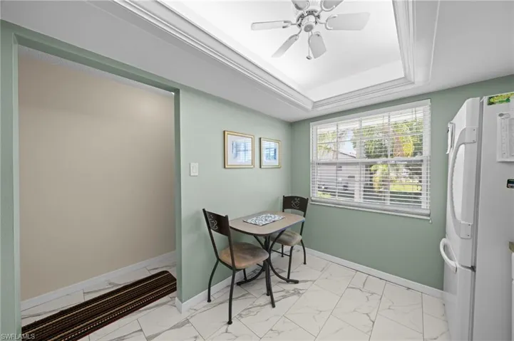 Kitchenette featuring a tray ceiling with a ceiling fan, a window with blinds, and white tile flooring