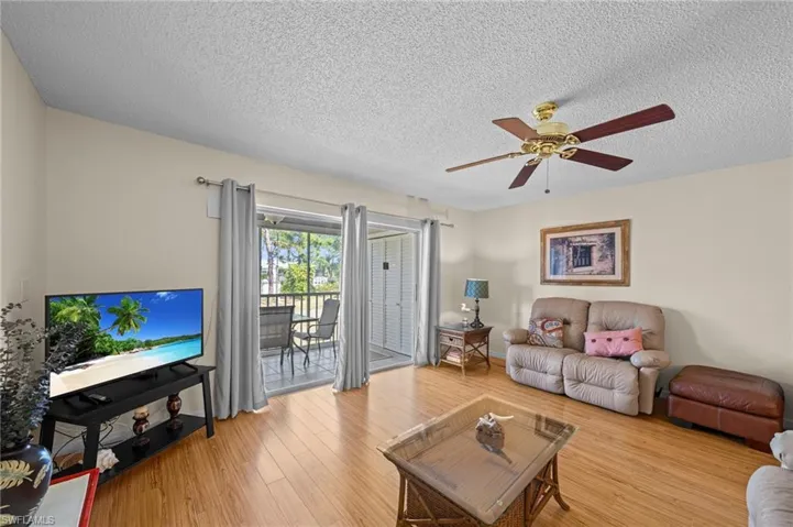 Living area with wood-finish flooring, a ceiling fan with integrated lighting, and a glass sliding door opening to a screened balcony
