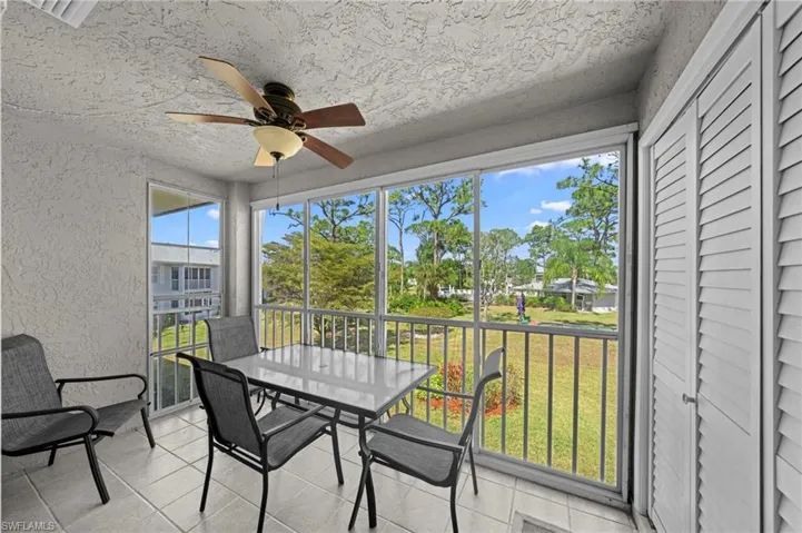 Screened balcony featuring tile flooring, a ceiling fan with light fixture, and louvered storage doors
