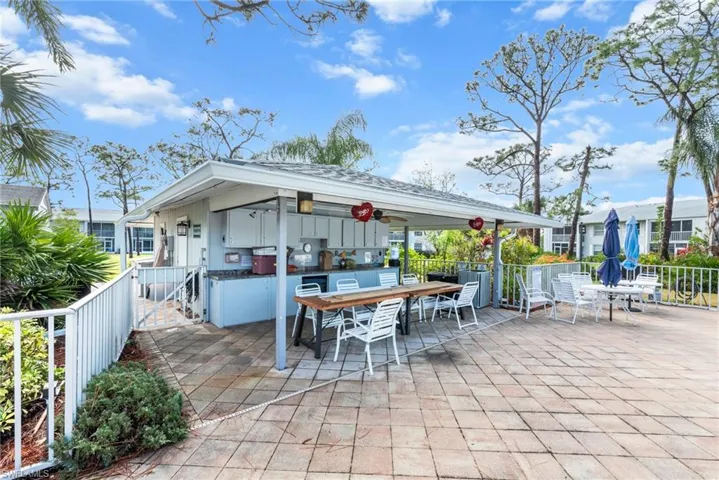 Outdoor covered patio with a built-in kitchen, extensive paver flooring, and mature landscaping