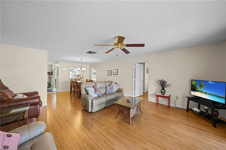 Spacious living area featuring wood-finish flooring, neutral wall tones, and a ceiling fan with integrated lighting