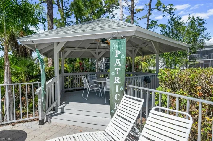 Covered gazebo structure with a shingled roof, featuring a raised deck and railing