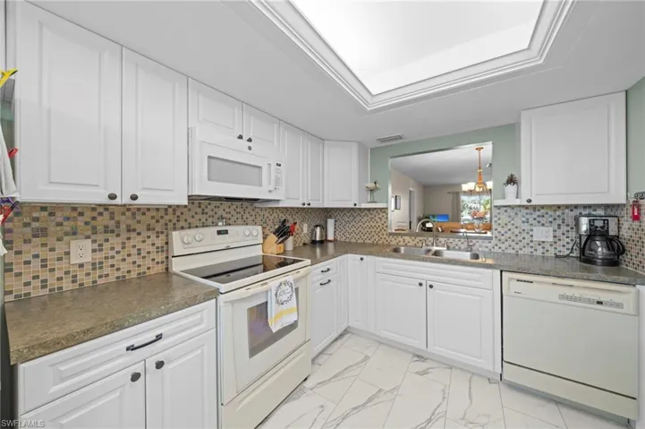 Kitchen featuring white paneled cabinetry, a mosaic tile backsplash, a pass-through window, and a skylight