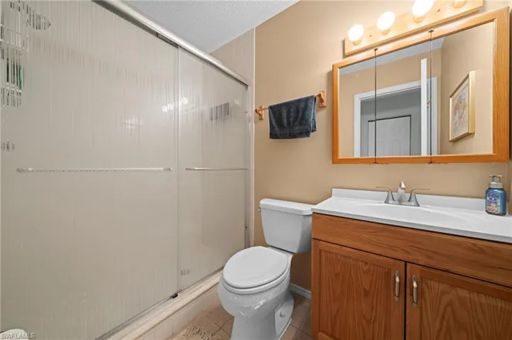 Full bathroom featuring a shower with sliding frosted glass doors, a single vanity with a white countertop and wood-finish cabinetry, a framed mirror with overhead vanity lighting, and neutral-toned wall paint