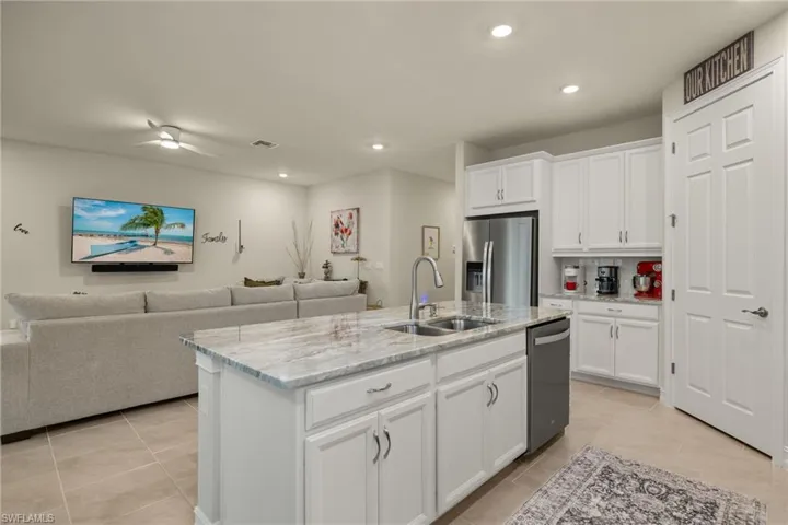 Kitchen featuring appliances with stainless steel finishes, sink, white cabinetry, light tile patterned flooring, and an island with sink