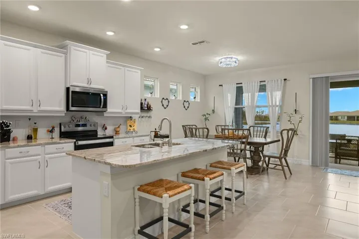 Kitchen with light stone countertops, white cabinets, appliances with stainless steel finishes, sink, and a kitchen island with sink
