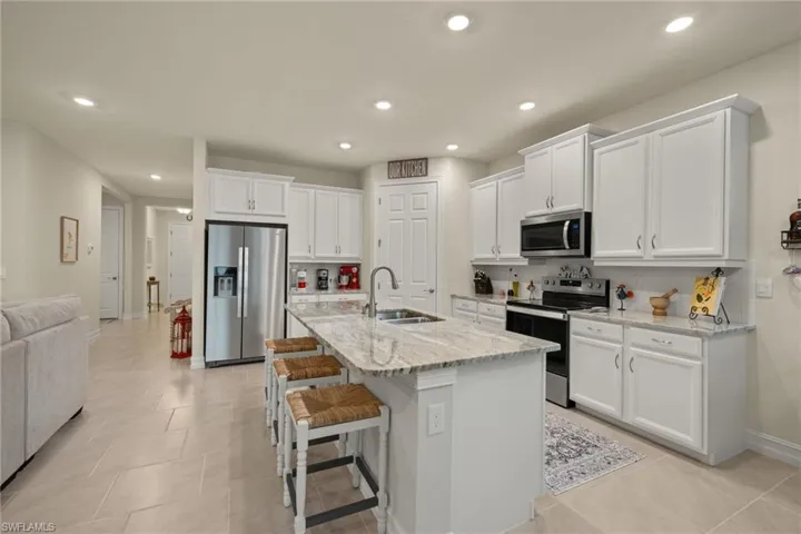 Kitchen with appliances with stainless steel finishes, sink, white cabinets, light stone counters, and a center island with sink