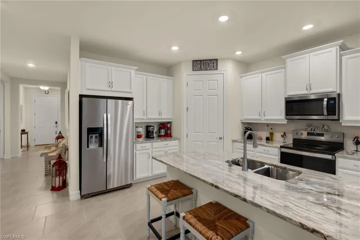 Kitchen featuring appliances with stainless steel finishes, sink, white cabinetry, light stone counters, and a breakfast bar