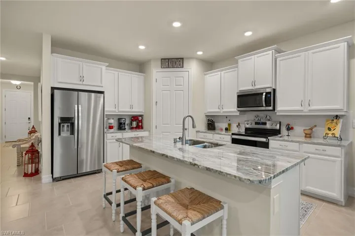 Kitchen with sink, stainless steel appliances, white cabinetry, and a kitchen island with sink