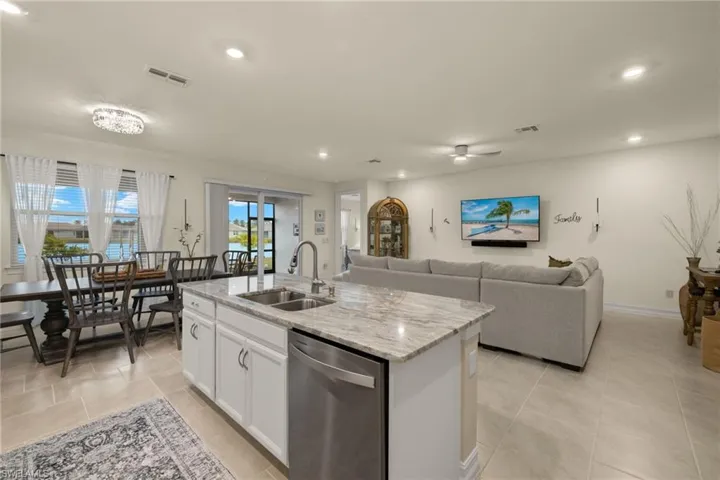 Kitchen with dishwasher, white cabinets, sink, an island with sink, and light stone counters