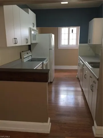 Galley kitchen featuring white cabinetry with dark hardware, white appliances including a range and microwave, light countertops, and wood-finish flooring