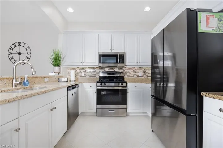 Kitchen with stainless steel appliances, light stone countertops, white cabinets, backsplash, and recessed lighting