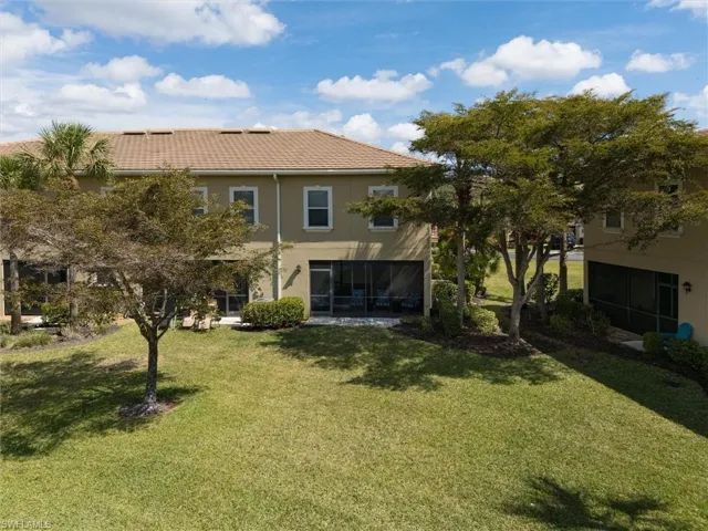 Rear view of house featuring a sunroom, a lawn, stucco siding, and a tile roof