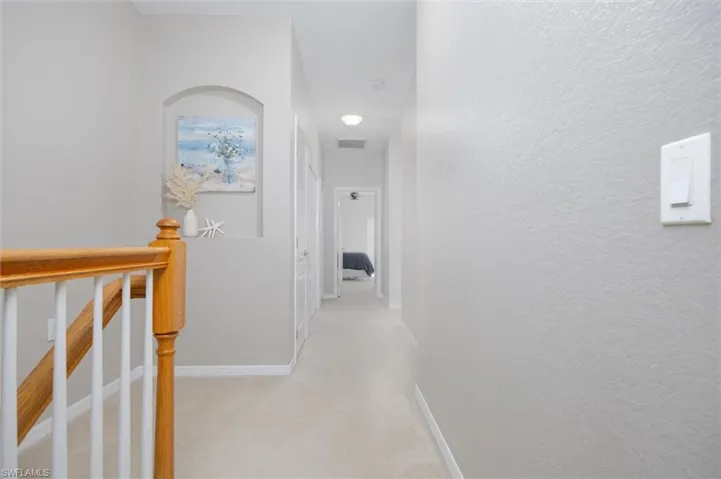 Hall with an upstairs landing, light carpet, and a textured wall