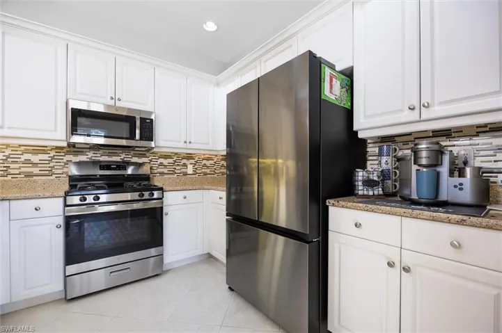 Kitchen featuring stainless steel appliances, white cabinets, light stone counters, and recessed lighting