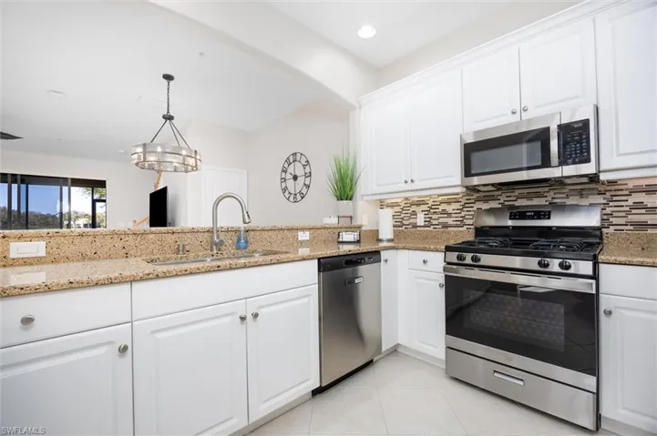 Kitchen featuring white cabinets, stainless steel appliances, light stone countertops, and tasteful backsplash