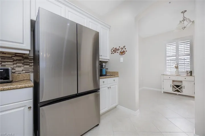 Kitchen with freestanding refrigerator, white cabinetry, and light stone counters