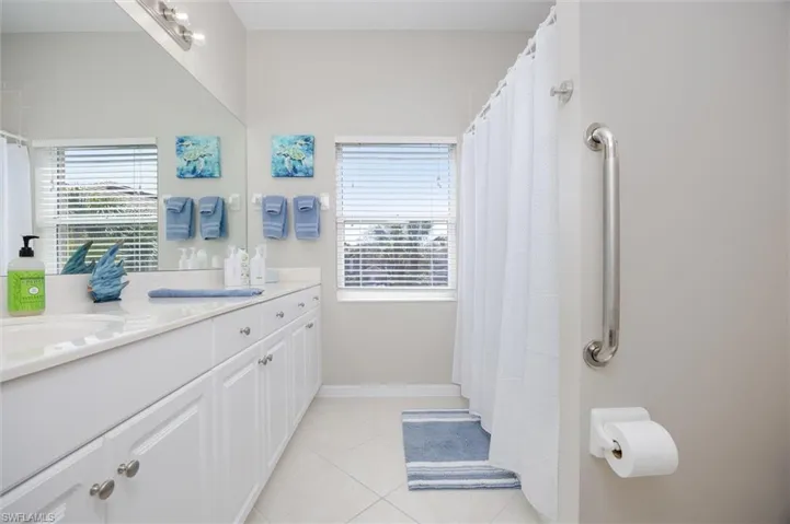 Bathroom with double vanity, a shower with curtain, plenty of natural light, and light tile patterned floors