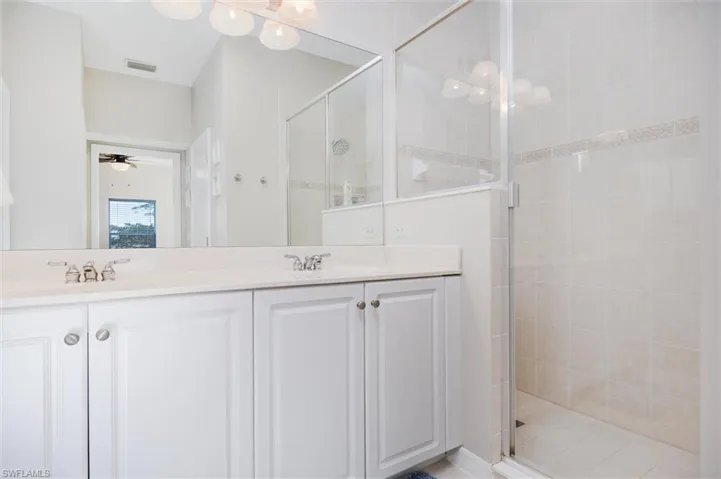Bathroom with double vanity, a stall shower, and a ceiling fan