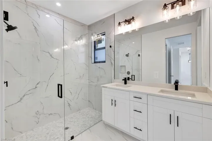 Full bath with double vanity, a marble finish shower, and light marble finish floors