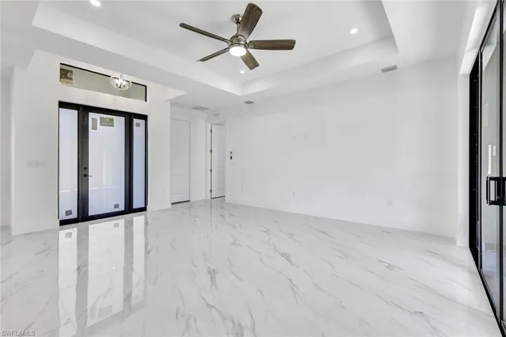 Empty room featuring a tray ceiling, recessed lighting, light marble finish flooring, and a ceiling fan