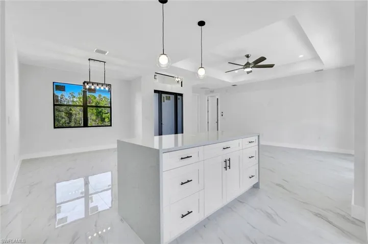 Kitchen with a tray ceiling, light marble finish flooring, white cabinets, decorative light fixtures, and light stone countertops