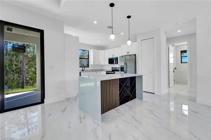 Kitchen with light marble finish flooring, white cabinets, decorative light fixtures, light stone counters, and appliances with stainless steel finishes
