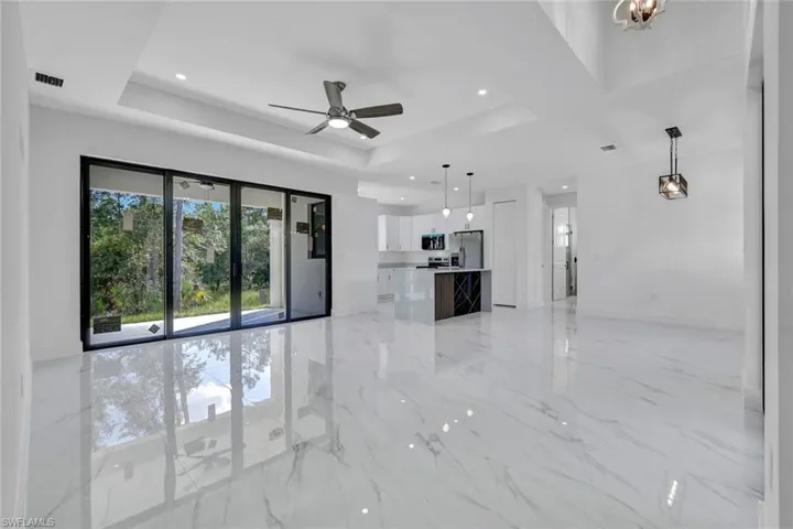 Unfurnished living room featuring light marble finish flooring, a tray ceiling, a ceiling fan, a chandelier, and recessed lighting