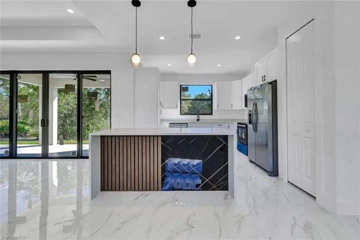 Kitchen featuring stainless steel fridge, light marble finish flooring, pendant lighting, light stone countertops, and white cabinetry