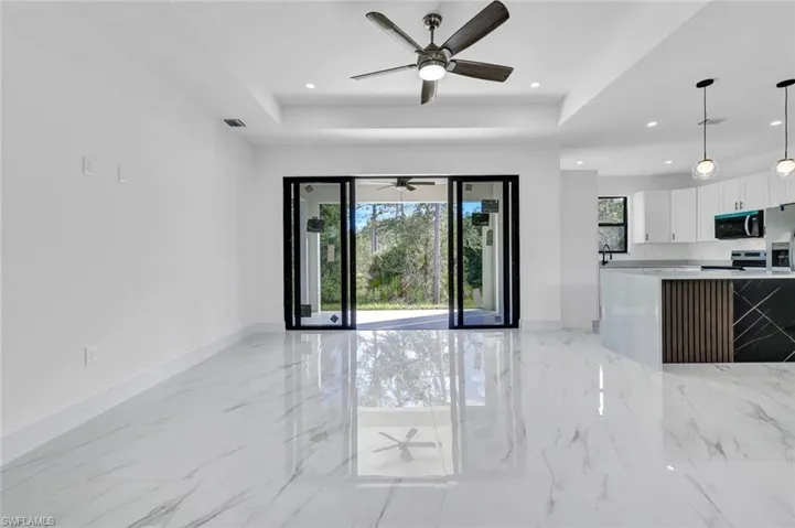 Unfurnished living room featuring a raised ceiling, light marble finish floors, recessed lighting, and a ceiling fan