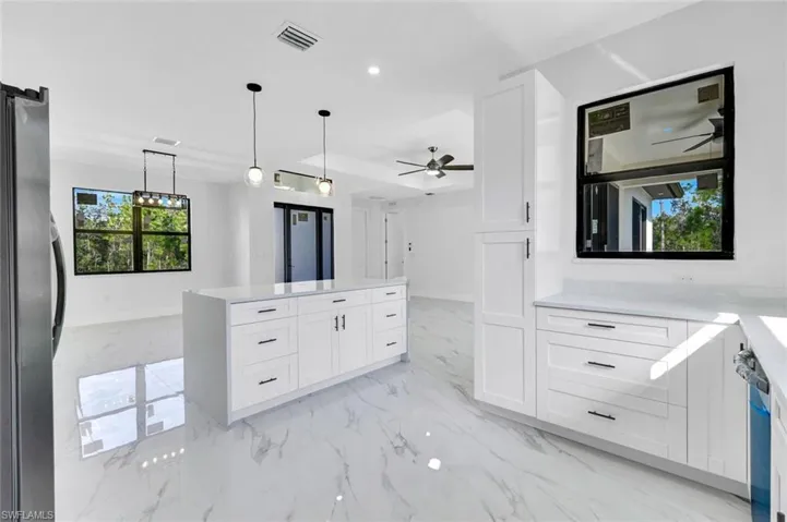 Kitchen featuring white cabinets, light stone counters, pendant lighting, freestanding refrigerator, and a center island