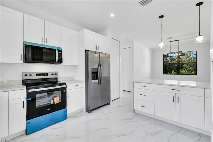Kitchen with stainless steel appliances, white cabinets, pendant lighting, light marble finish flooring, and recessed lighting