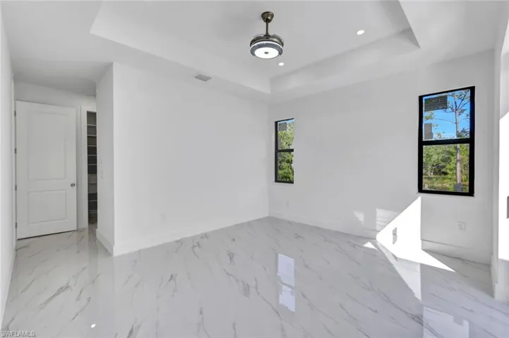 Unfurnished room with a tray ceiling, light marble finish flooring, and recessed lighting