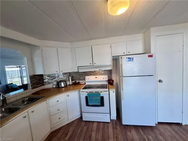 Kitchen featuring under cabinet range hood, white appliances, a sink, white cabinetry, and dark wood finished floors