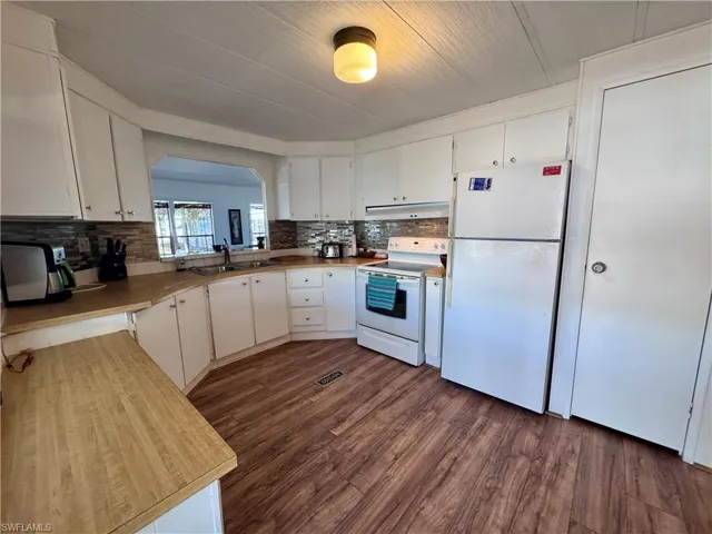 Kitchen with dark wood finished floors, tasteful backsplash, white cabinets, a sink, and white appliances
