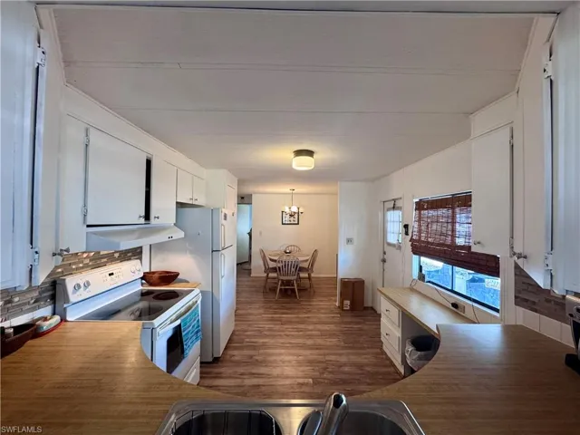 Kitchen with a notable chandelier, under cabinet range hood, white appliances, dark wood-style flooring, and white cabinets