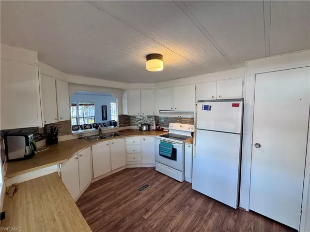Kitchen featuring white appliances, a sink, white cabinets, dark wood-style floors, and tasteful backsplash