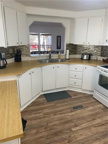 Kitchen with backsplash, range, white cabinetry, and dark wood-type flooring