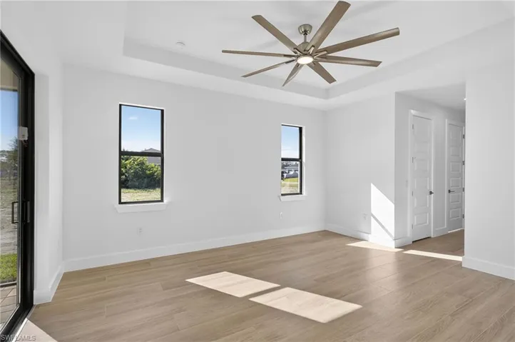 Unfurnished room featuring a raised ceiling, light wood-style flooring, and a ceiling fan