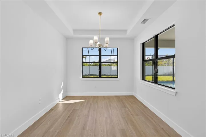 Unfurnished dining area featuring a chandelier, light wood-style floors, and a raised ceiling