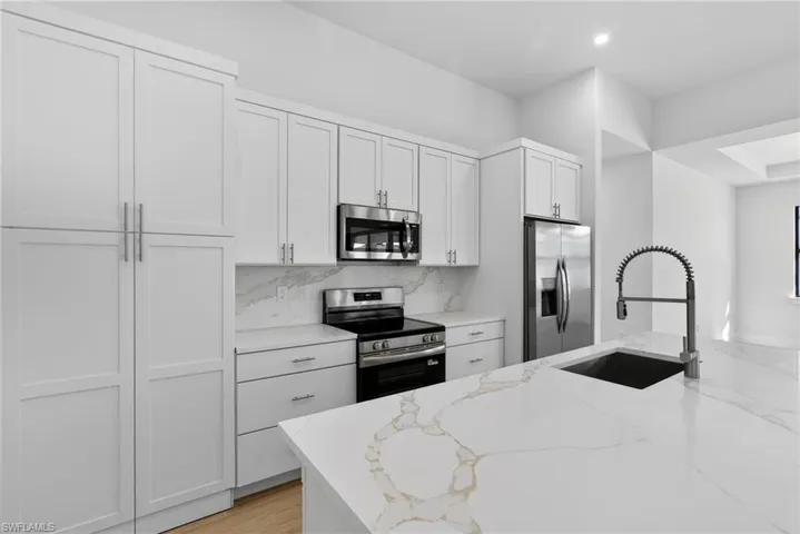 Kitchen featuring stainless steel appliances, light stone countertops, white cabinets, decorative backsplash, and recessed lighting