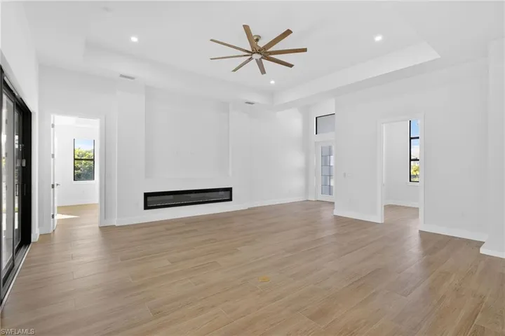 Unfurnished living room featuring a raised ceiling, healthy amount of natural light, a glass covered fireplace, light wood-style floors, and recessed lighting