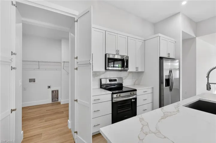Kitchen with stainless steel appliances, white cabinetry, light stone counters, and light wood finished floors