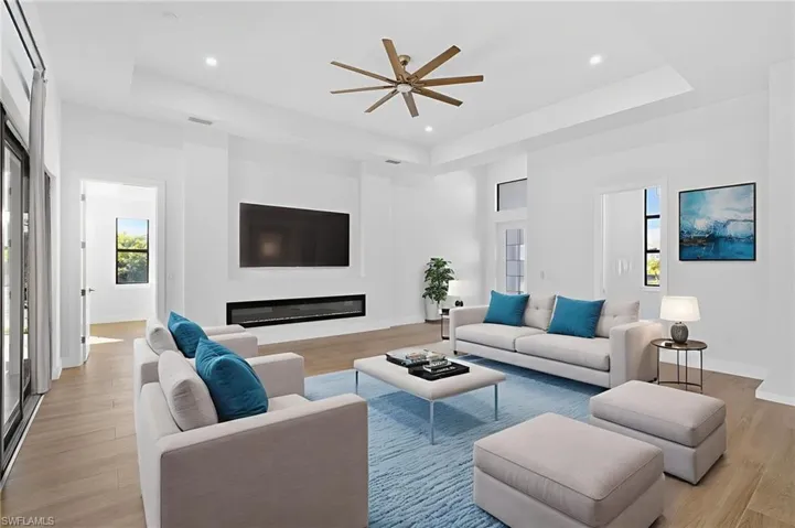 Living area with a tray ceiling, a glass covered fireplace, ceiling fan, light wood-type flooring, and recessed lighting