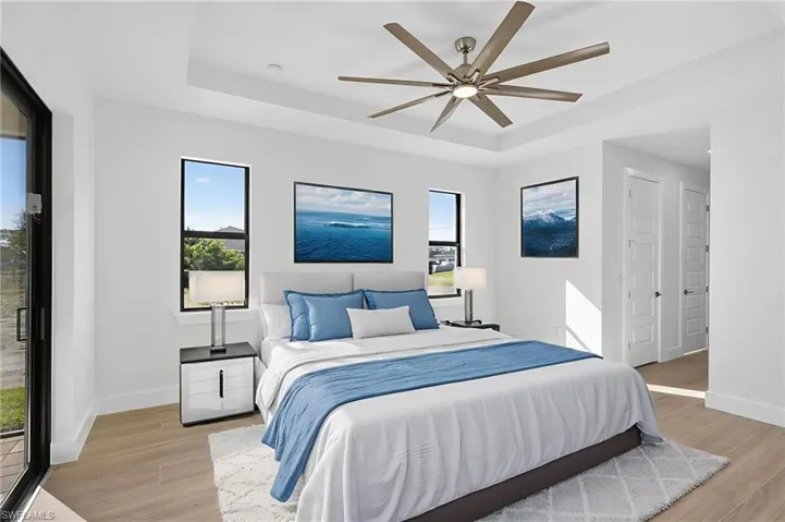 Bedroom featuring a tray ceiling, multiple windows, light wood-type flooring, and a ceiling fan